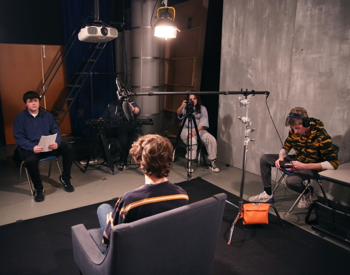 Several students sit in a video production studio. 