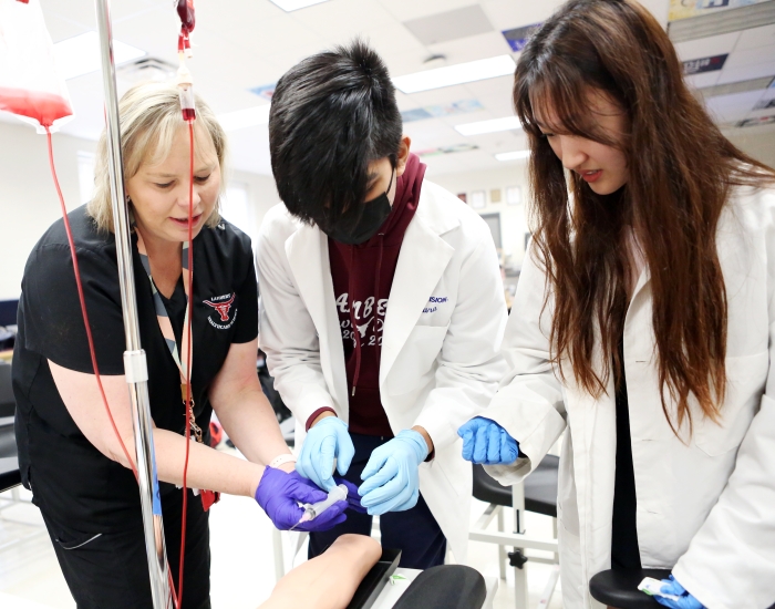 Students work with an instructor to practice a medical task. 