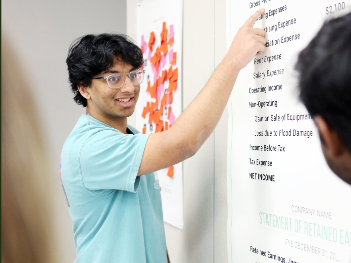 A student points at a poster listing business terms. 