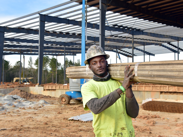 A student holds lumber on construction site. 